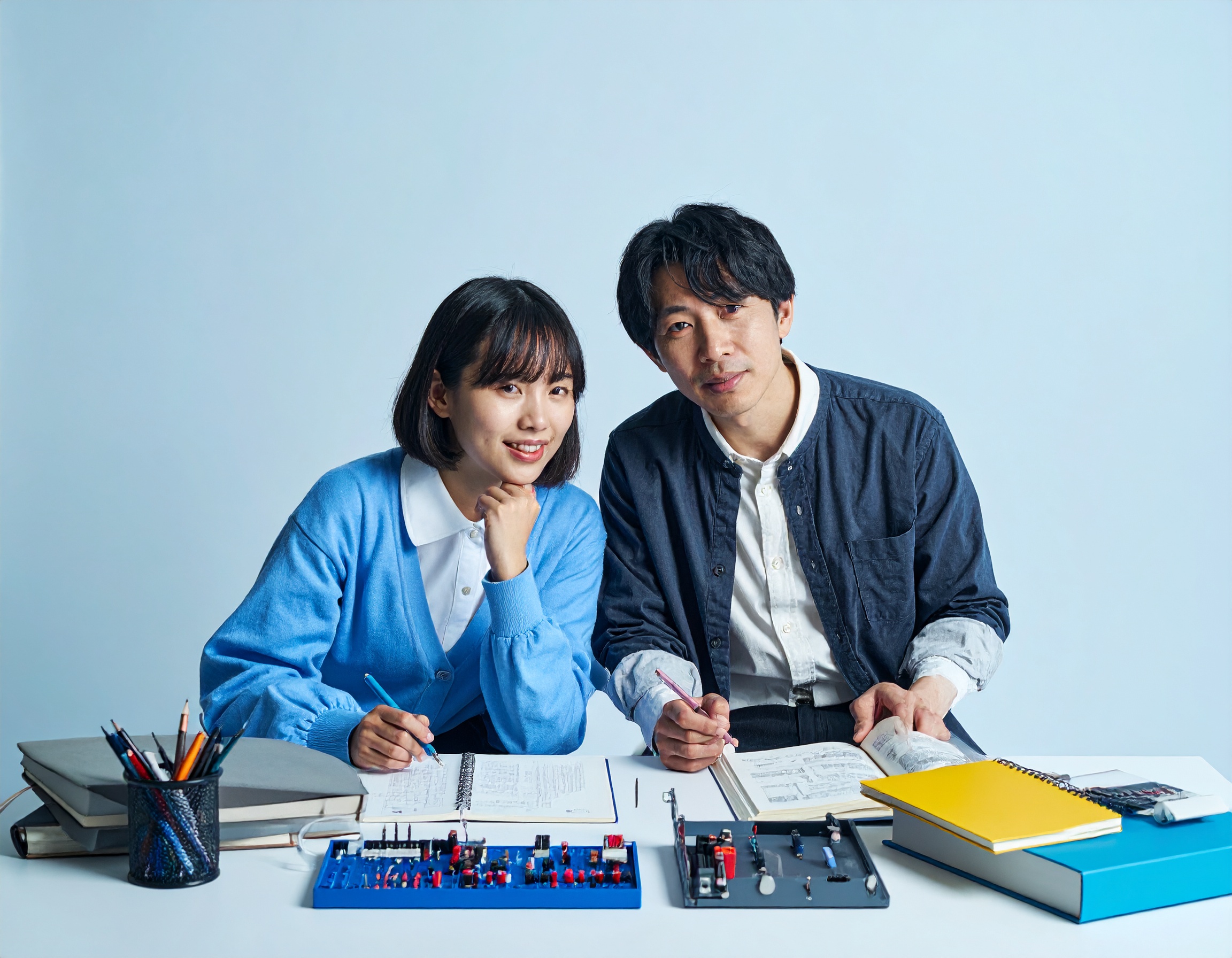 電験三種の勉強をしている日本人男性と女性。 参考書やノート、電気回路の教材を広げて学習している様子。 独学とオンライン学習を比較しているイメージ。